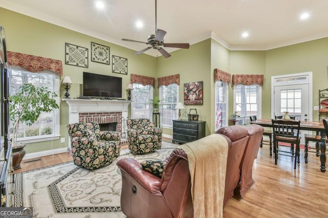 living room featuring ornamental molding, ceiling fan, light hardwood / wood-style flooring, a fireplace, and a high ceiling