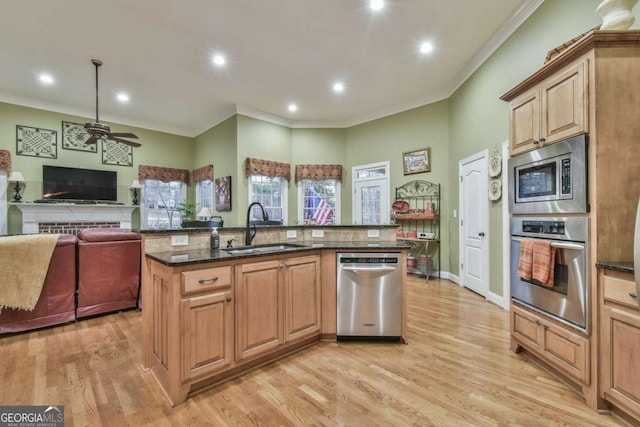 kitchen with a kitchen island with sink, sink, light wood-type flooring, and appliances with stainless steel finishes