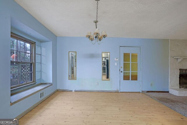 unfurnished dining area featuring an inviting chandelier, a fireplace, a textured ceiling, and light wood-type flooring