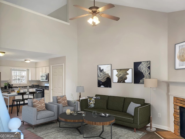 living area with ceiling fan, baseboards, a stone fireplace, a towering ceiling, and dark wood-style floors