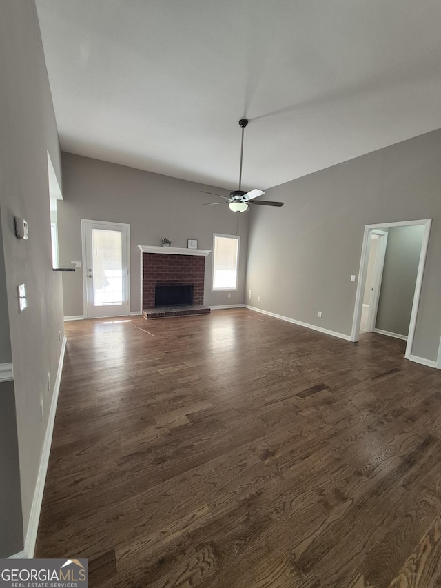 unfurnished living room featuring a brick fireplace, ceiling fan, and dark wood-type flooring