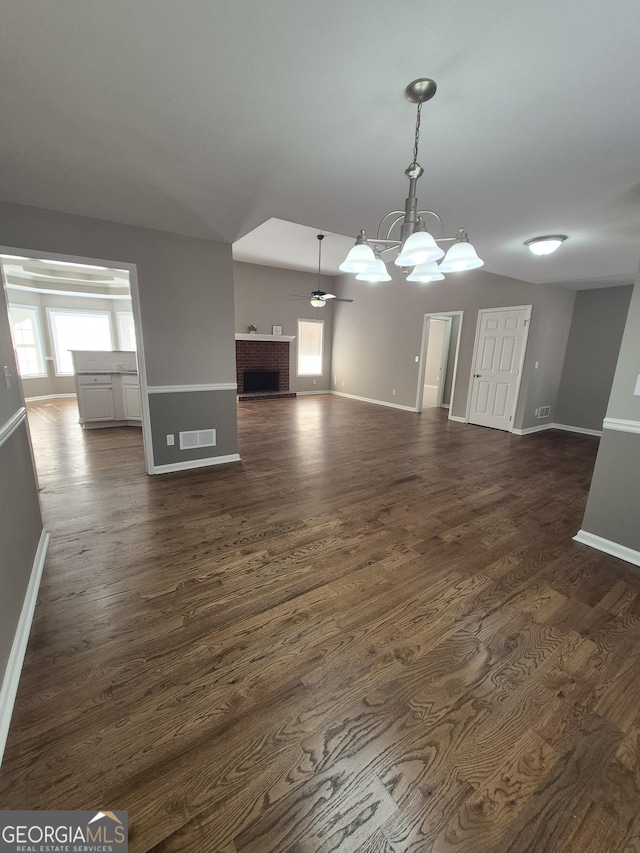 unfurnished living room featuring ceiling fan with notable chandelier, dark hardwood / wood-style floors, and a brick fireplace