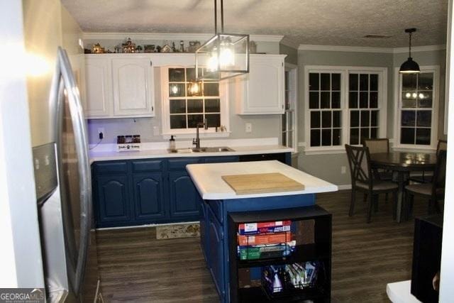 kitchen featuring stainless steel fridge, blue cabinets, sink, white cabinetry, and hanging light fixtures