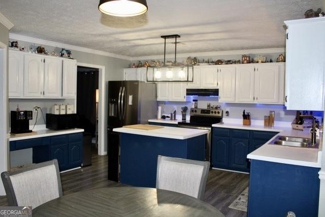 kitchen with dark wood finished floors, ornamental molding, under cabinet range hood, white cabinetry, and a sink