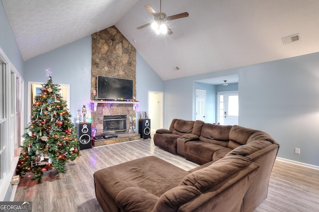 living room with lofted ceiling, a stone fireplace, ceiling fan, a textured ceiling, and light hardwood / wood-style floors