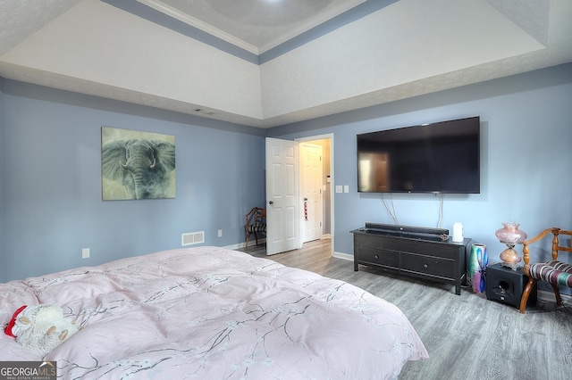 bedroom with light hardwood / wood-style floors, a raised ceiling, and ornamental molding