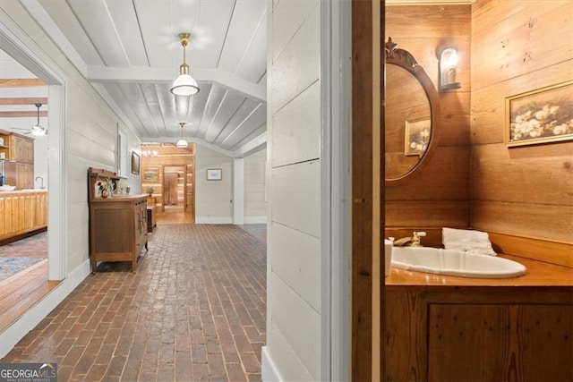 hallway featuring sink, vaulted ceiling, and wood walls