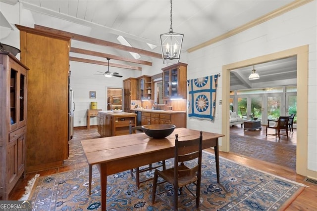 dining space with ceiling fan with notable chandelier, beam ceiling, ornamental molding, and dark wood-type flooring