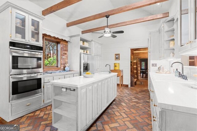 kitchen featuring a center island with sink, sink, beamed ceiling, and stainless steel appliances