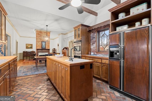 kitchen with stainless steel double oven, paneled fridge, an island with sink, decorative light fixtures, and ornamental molding