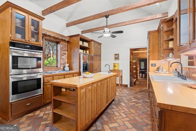 kitchen with wood counters, built in fridge, sink, an island with sink, and stainless steel double oven