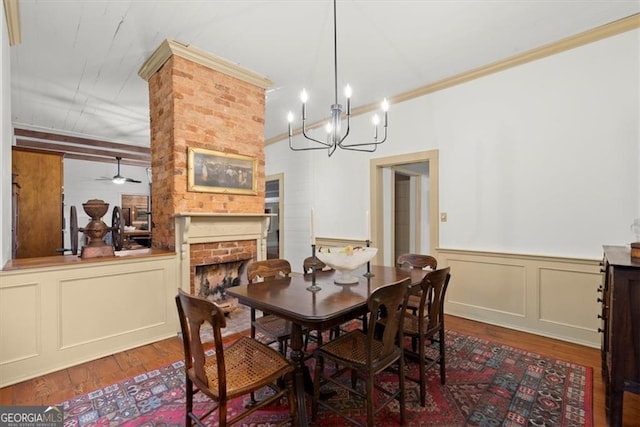 dining room with a fireplace, hardwood / wood-style floors, ceiling fan with notable chandelier, and ornamental molding