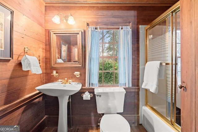 bathroom featuring wood-type flooring, toilet, wooden walls, and enclosed tub / shower combo