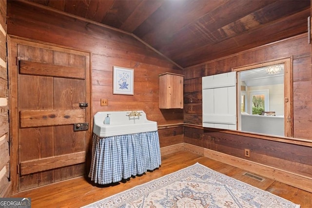 living area featuring light wood-type flooring, wood ceiling, sink, lofted ceiling, and wood walls