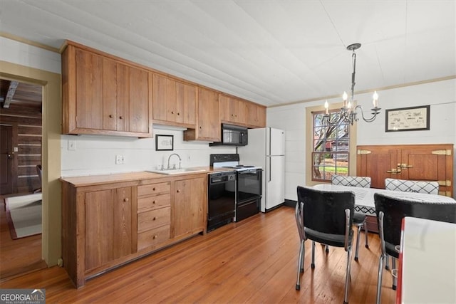 kitchen with black appliances, sink, hanging light fixtures, a notable chandelier, and light hardwood / wood-style floors