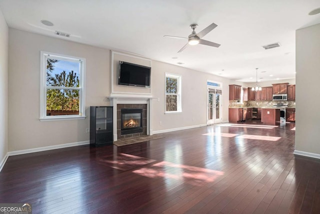 unfurnished living room featuring a tiled fireplace, dark hardwood / wood-style flooring, and ceiling fan with notable chandelier