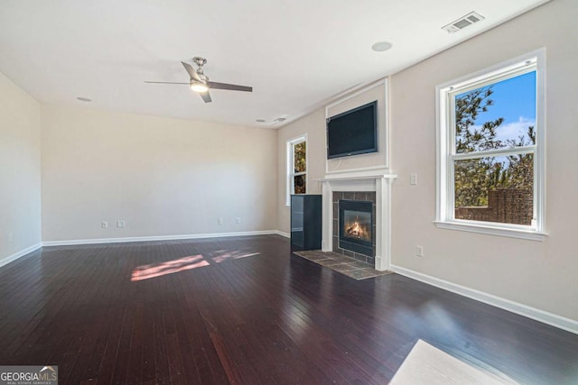 unfurnished living room with a fireplace, dark hardwood / wood-style floors, ceiling fan, and a healthy amount of sunlight