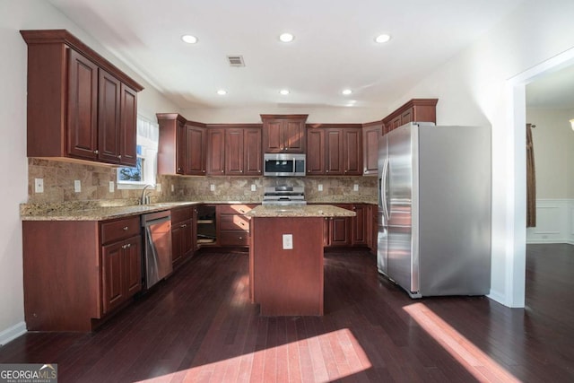 kitchen featuring a kitchen island, dark hardwood / wood-style flooring, light stone countertops, and stainless steel appliances