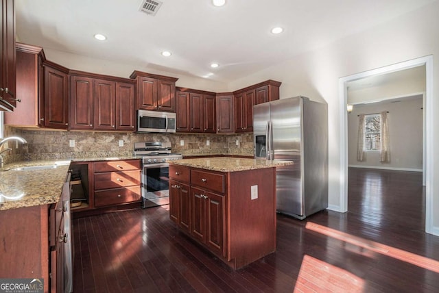 kitchen featuring light stone countertops, stainless steel appliances, dark wood-type flooring, sink, and a center island