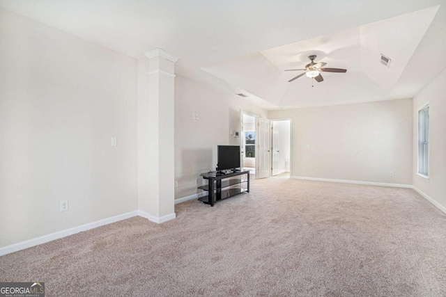 unfurnished living room featuring a raised ceiling, ceiling fan, decorative columns, and light carpet