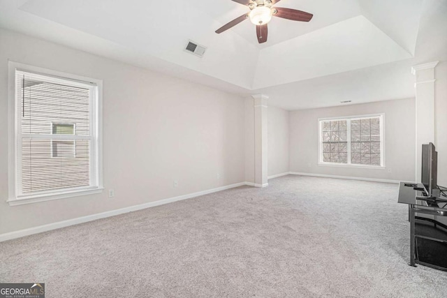 unfurnished living room with a raised ceiling, ceiling fan, light colored carpet, and ornate columns