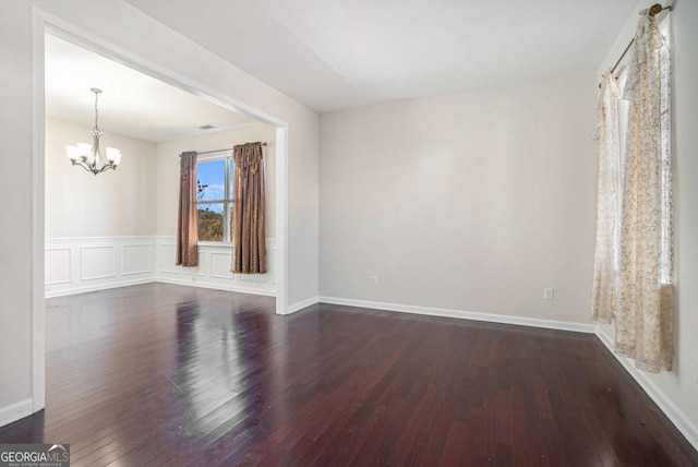 spare room with dark hardwood / wood-style flooring and an inviting chandelier