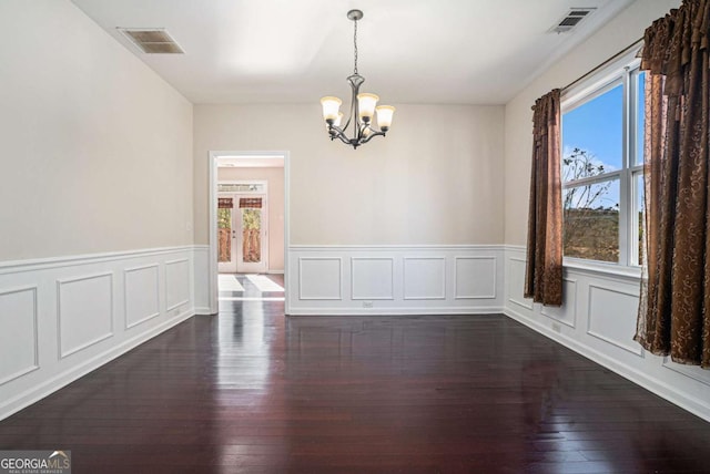 spare room with plenty of natural light, dark hardwood / wood-style floors, and an inviting chandelier