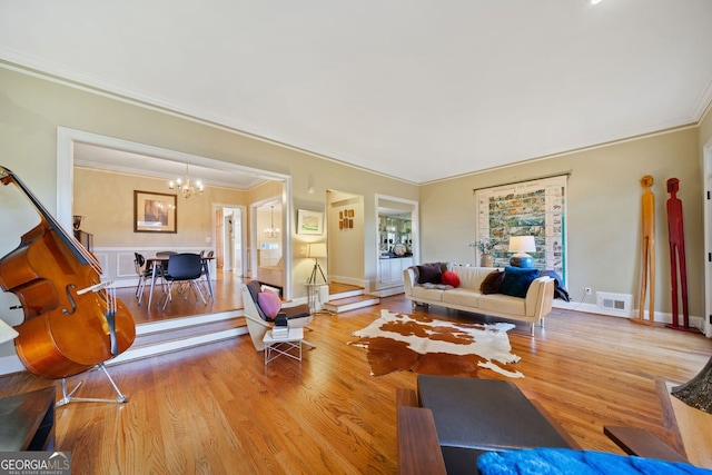 living room featuring an inviting chandelier, ornamental molding, and light hardwood / wood-style flooring