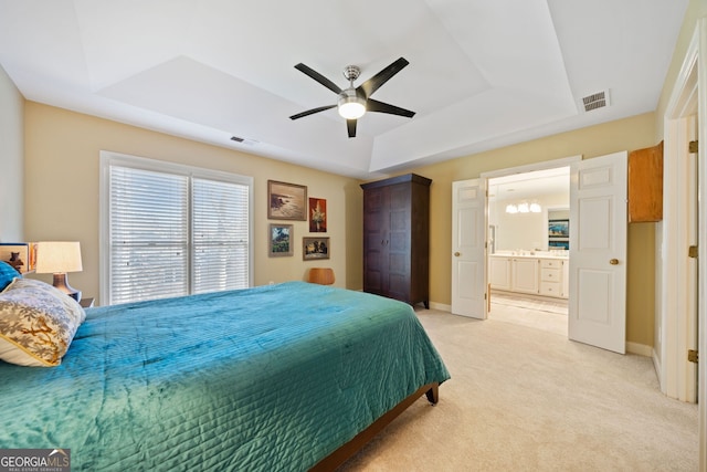 bedroom with a tray ceiling, connected bathroom, ceiling fan, and light carpet