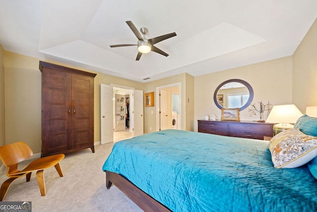 bedroom with ceiling fan, a raised ceiling, washer / clothes dryer, light carpet, and a closet