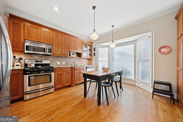 kitchen with crown molding, hanging light fixtures, light hardwood / wood-style flooring, appliances with stainless steel finishes, and light stone counters