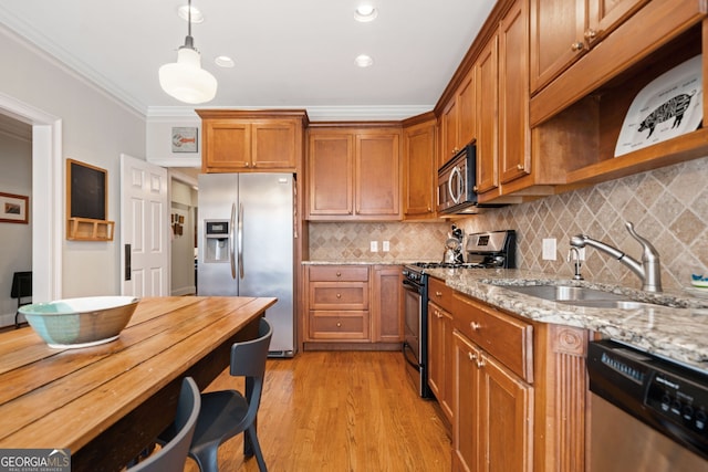 kitchen with sink, light hardwood / wood-style flooring, light stone countertops, appliances with stainless steel finishes, and decorative light fixtures