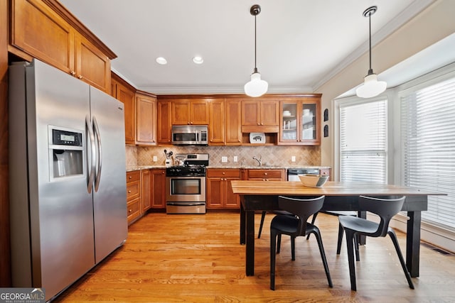 kitchen with crown molding, stainless steel appliances, decorative light fixtures, and light hardwood / wood-style floors