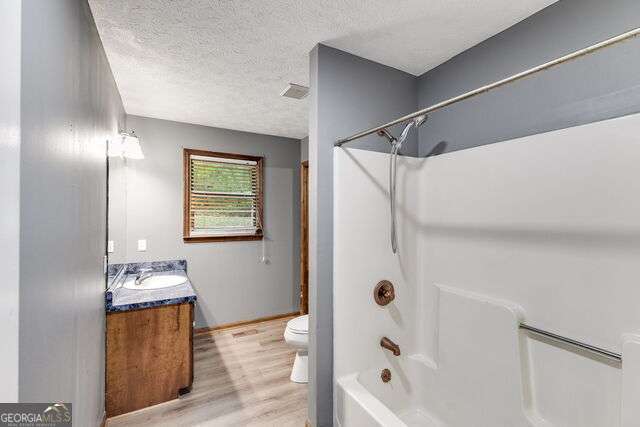 full bathroom featuring vanity, shower / washtub combination, toilet, a textured ceiling, and wood-type flooring