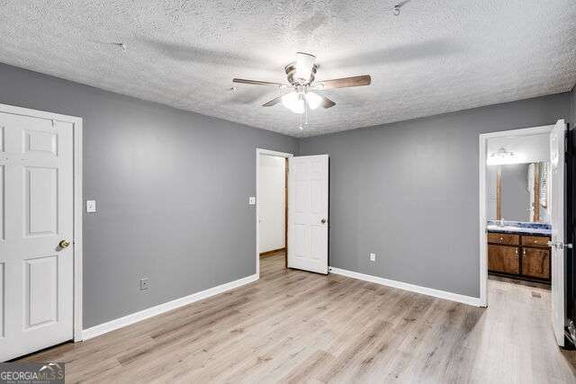 unfurnished bedroom with connected bathroom, ceiling fan, a textured ceiling, and light wood-type flooring