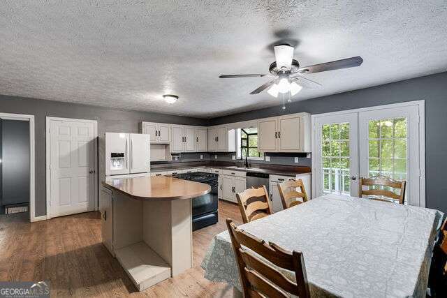 kitchen featuring white cabinetry, black range with electric cooktop, white refrigerator with ice dispenser, wood-type flooring, and a kitchen island