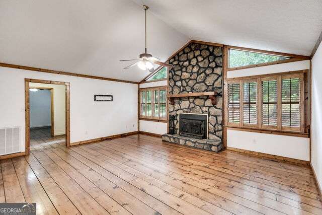 unfurnished living room featuring a stone fireplace, light hardwood / wood-style flooring, a healthy amount of sunlight, and lofted ceiling