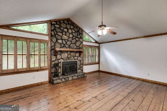 unfurnished living room featuring plenty of natural light, vaulted ceiling, a stone fireplace, and light hardwood / wood-style flooring