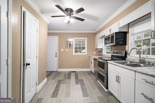 kitchen with white cabinets, sink, light hardwood / wood-style flooring, ornamental molding, and appliances with stainless steel finishes