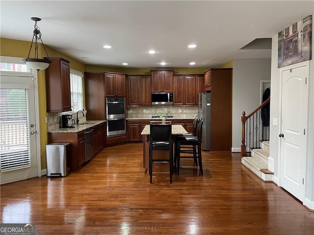 kitchen with a center island, dark wood-type flooring, appliances with stainless steel finishes, decorative light fixtures, and light stone counters