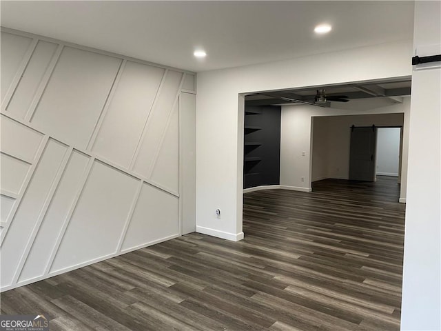 basement with a barn door, ceiling fan, and dark hardwood / wood-style floors