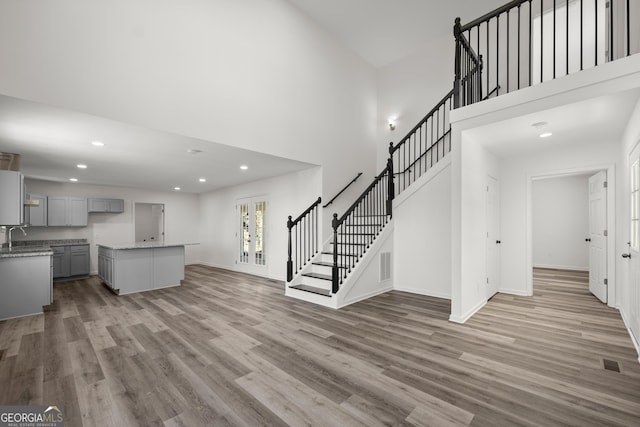 unfurnished living room with sink, a towering ceiling, and light hardwood / wood-style floors