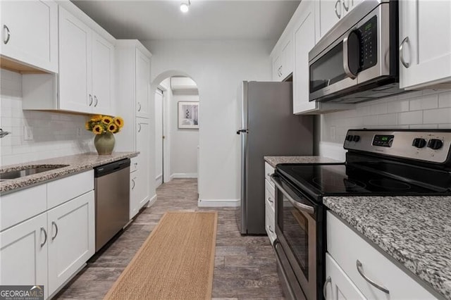 kitchen with white cabinets, light stone counters, dark wood-type flooring, and appliances with stainless steel finishes