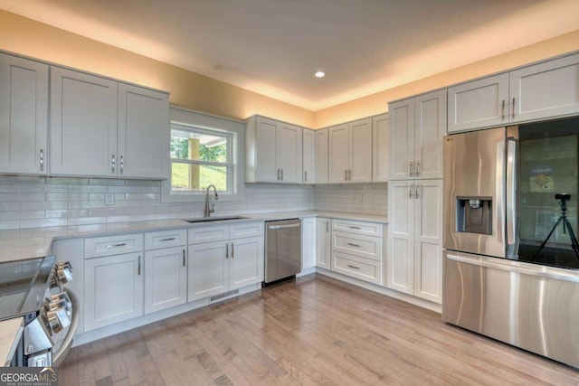 kitchen with decorative backsplash, sink, stainless steel appliances, and light hardwood / wood-style flooring