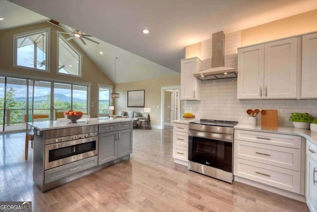 kitchen featuring backsplash, stainless steel appliances, wall chimney range hood, light hardwood / wood-style flooring, and white cabinets