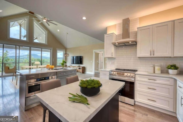 kitchen with a center island, stainless steel appliances, light hardwood / wood-style flooring, and wall chimney range hood