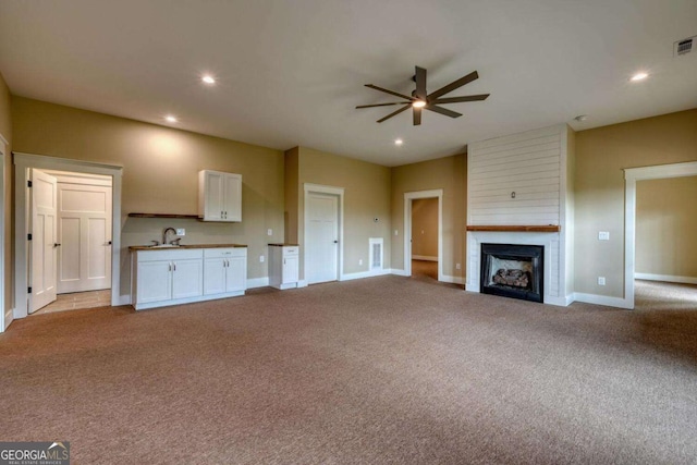 unfurnished living room with a fireplace, light colored carpet, ceiling fan, and sink