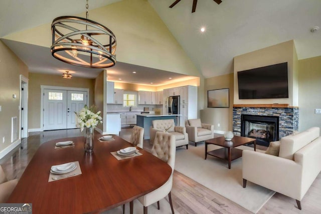 dining room with high vaulted ceiling, a stone fireplace, sink, light hardwood / wood-style floors, and a chandelier