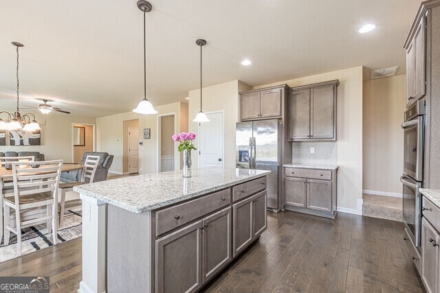 kitchen with light stone countertops, a center island, stainless steel appliances, dark hardwood / wood-style flooring, and decorative light fixtures