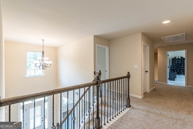 hallway featuring light carpet and a notable chandelier